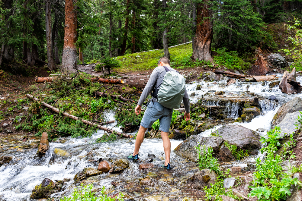 Hiker crosses a rushing river over wet rocks after snowmelt.