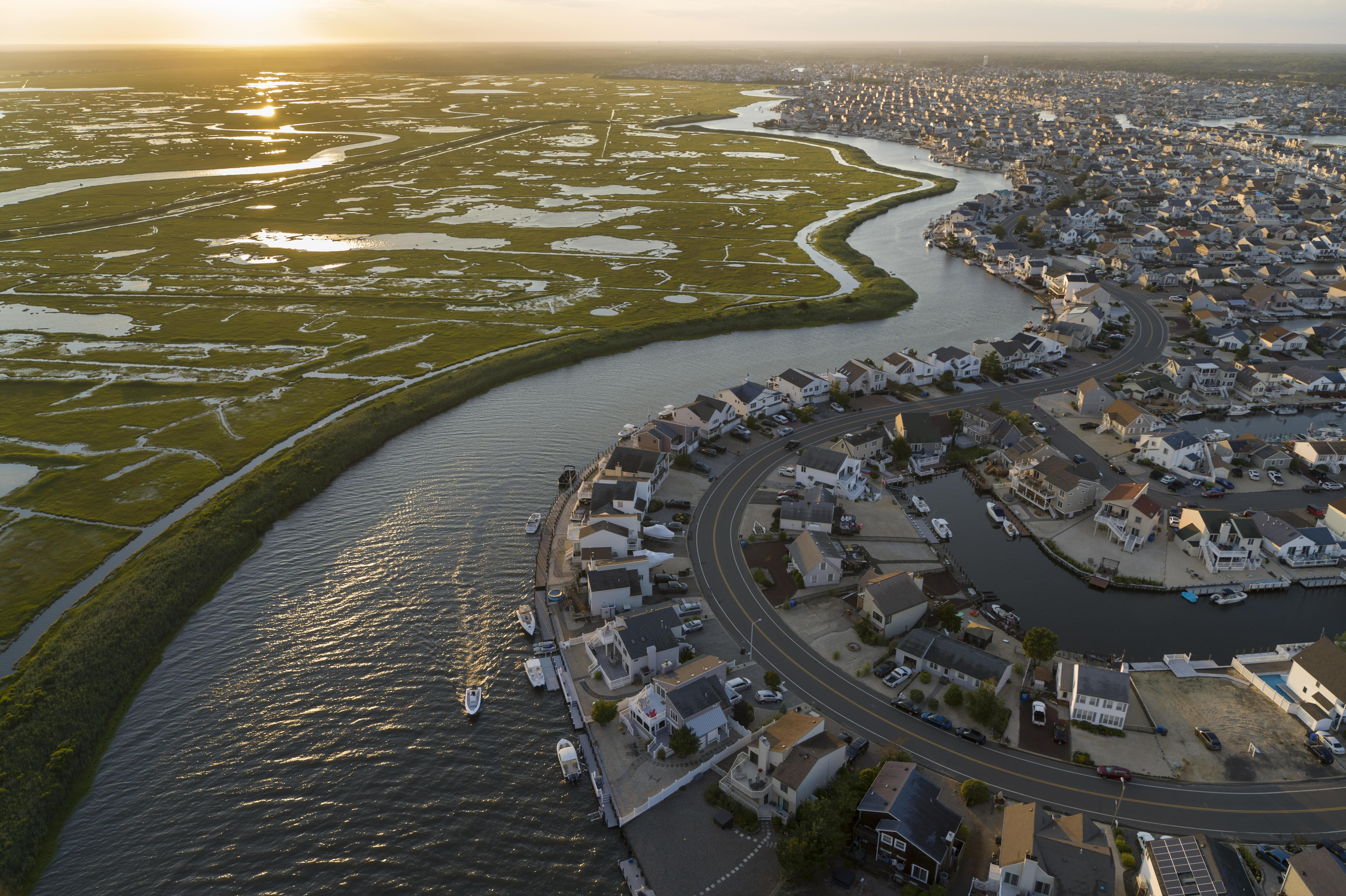 A river flows toward the sea with flat wetlands on one side and housing and development on the other side.